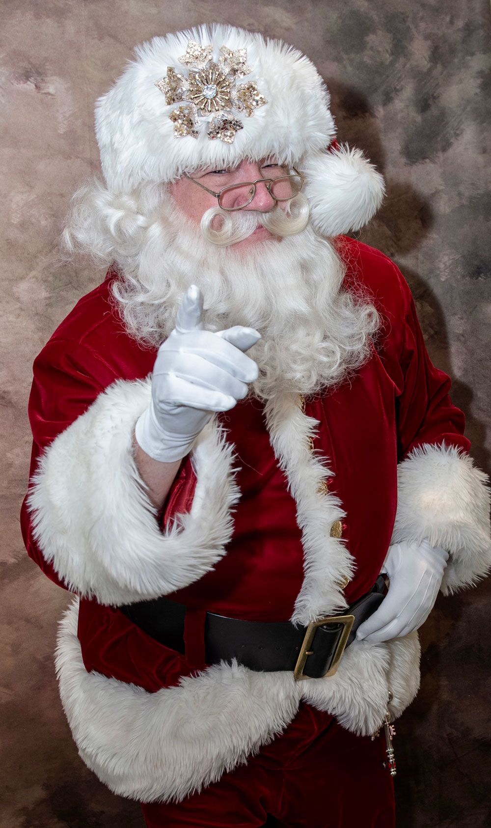 Santa Joe in his red velvet suit and white gloves, smiling and pointing at the camera