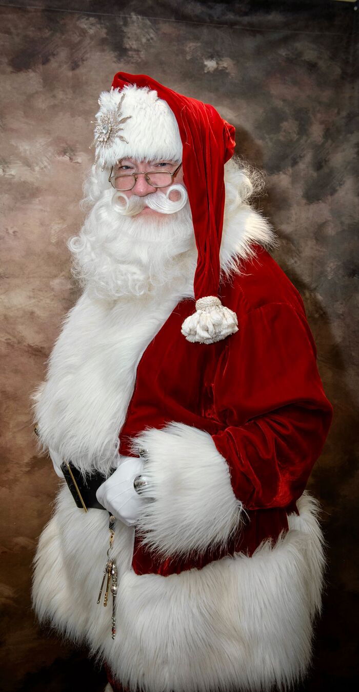 Santa Joe standing in profile in his fur-trimmed coat and long red hat